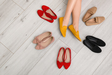 Wall Mural - Woman's legs among flat shoes on white wooden background