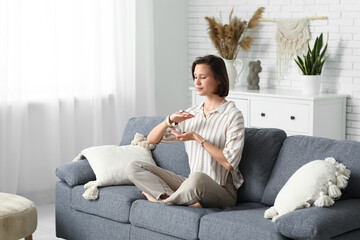 Poster - Young woman meditating while sitting on sofa at home