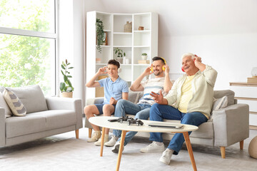 Wall Mural - Teenage boy with his dad and grandfather in headphones sitting on sofa at home