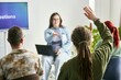 © Seventyfour - Group of participants engaging in interactive business seminar, with one individual raising hand while seated and another person presenting in background with laptop