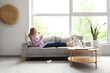 © Pixel-Shot - Ill young woman with thermometer and tissue sneezing on sofa at home