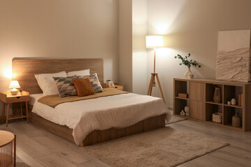 Poster - Stylish interior of bedroom with comfortable bed, lamp and shelving unit at evening