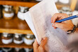 © Penn/peopleimages.com - Hands, shop owner and writing with paperwork in cafe with review for inventory, stock and ingredients. Person, documents and checklist with notes by shelf for coffee, tea and stats at restaurant