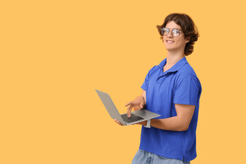 Male programmer in eyeglasses working with laptop on orange background