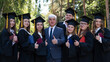 © Михаил Решетников - University professor and seven students rejoice at graduation and show thumbs up outdoors.