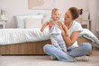 © Pixel-Shot - Beautiful young happy mother with cute little baby sitting on floor in bedroom at home