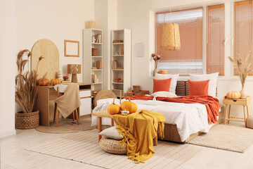 Poster - Interior of stylish bedroom with comfortable workplace, coffee table, plaid and pumpkins