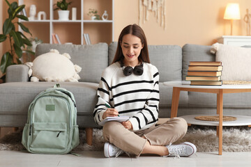 Poster - Beautiful happy female student with stack of books, backpack and headphones studying on floor at home