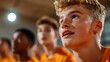 © LifeMedia - A focused young basketball player with a blond hair sitting among teammates, attentively watching something, highlighting the concentration and eagerness in their expressions.