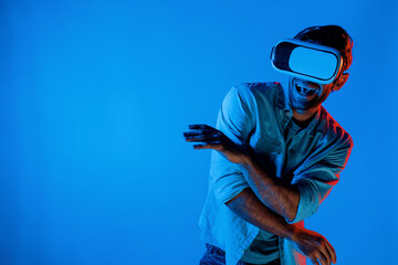 Handsome smart man dancing and moving gesture to music by using VR glasses with neon light background. Caucasian male gamer standing while moving to pop music wearing technology innovation. Deviation.