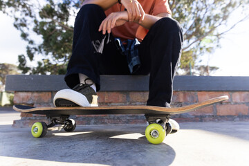 Sitting on skateboard, asian teenage boy hanging out outdoors in casual attire