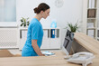 © New Africa - Professional receptionist working at wooden desk in hospital