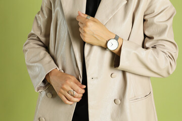 Beautiful woman in stylish beige jacket and watch on olive background, closeup