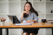 © Kritdanai - Focused Businesswoman:  A young Asian businesswoman sits at her desk, reviewing documents and data on her tablet, exuding a focused and determined work ethic in a modern office setting.  She is a symb