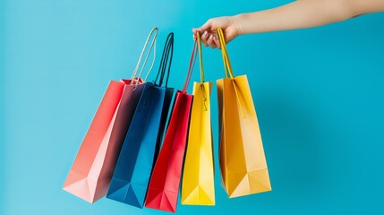 Female hand holding multiple colorful shopping bags against a vibrant blue background, ideal for e-commerce, retail marketing, and online shopping promotions, featuring bright, eye-catching colors per