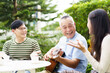 © DG PhotoStock - Happy Asian family spending time together, man and woman let their father playing a guitar and singing in backyard garden at home. Mental health care and wellbeing in senior adult.