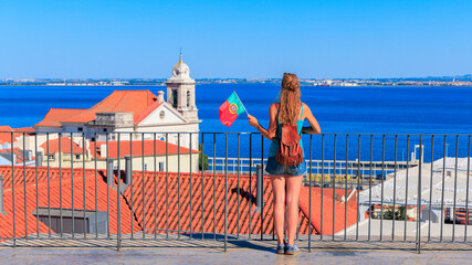 Wall Mural - Travel destination in Portugal- Woman holding Portuguese flag enjoys panoramic view of ocean and rooftop Lisbon