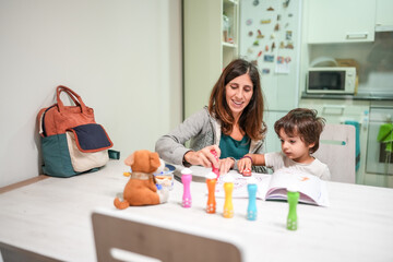 A woman and a child are sitting at a table with a book and a bag