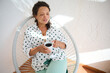 © Taras Grebinets - Relaxed woman enjoying a cup of coffee in a bright room, wearing a polka dot shirt and seated comfortably in a chair