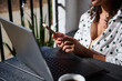 © Taras Grebinets - Woman working on a laptop and smartphone at an outdoor table, enjoying coffee and sunlight