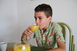 © Taras Grebinets - Young boy in a tiger-print shirt enjoying a refreshing glass of orange juice at the dining table