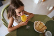 © Taras Grebinets - Young girl enjoying a refreshing glass of orange juice at the breakfast table with bread and a cup