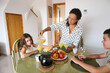 © Taras Grebinets - Mother pouring juice for her children during a family breakfast with fresh fruits in a cozy home setting