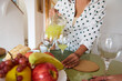 © Taras Grebinets - Woman pouring fresh juice in an elegant kitchen setting with fruit and bread in a relaxed atmosphere