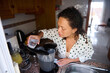 © Taras Grebinets - Woman preparing a blend of fresh ingredients in a kitchen setting, pouring water into a blender for a homemade recipe creation