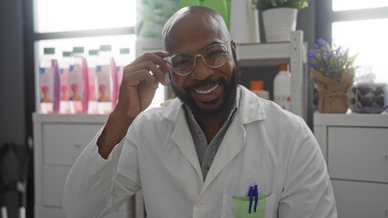 Handsome young man with glasses and beard smiling in a pharmacy wearing a white coat