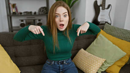 Poster - Surprised young woman in sweater pointing at herself indoors with guitar in background.