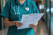 © syhin_stas - Confident female doctor in blue scrubs holds clipboard with medical records in hospital corridor, ready to provide care