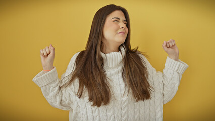 Wall Mural - A joyful young hispanic woman in a white sweater dances over a yellow background.