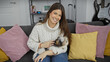 © Krakenimages.com - Hispanic woman smiling, holding a biewer terrier in a cozy living room with colorful pillows.