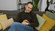 © Krakenimages.com - Young hispanic man checks his smartwatch comfortably at home, surrounded by a cozy decor with cushions and a guitar.