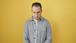© Krakenimages.com - Hispanic man in grey shirt posing with a stern expression against a plain yellow background, depicting a serious adult male.