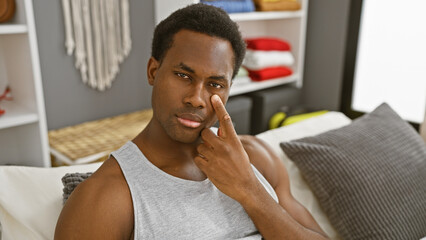 Wall Mural - A thoughtful young african american man in a casual indoor bedroom setting touching his face.