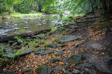 Path along stony river at junction of summer and autumn