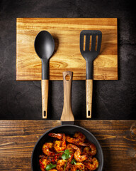 black ladles with wooden handle and pan on black and wooden background