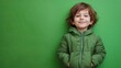 © Pricha.RT - A cheerful child dressed in a green jacket standing in front of a bright green backdrop, smiling confidently.