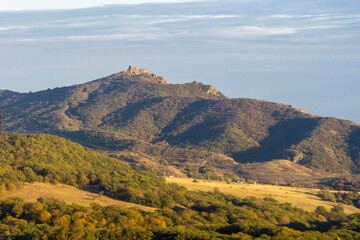 Azeula Kojori fortress on a mountain covered with autumn trees illuminated by sunlight. Valley, fields and hills in the foreground