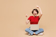© ViDi Studio - Full body young happy IT woman she wear red t-shirt casual clothes sits hold use work on laptop pc computer point finger aside isolated on plain pastel light beige background studio Lifestyle concept