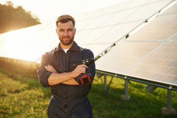 Arms crossed, standing. Man is working with solar panels outdoors at daytime