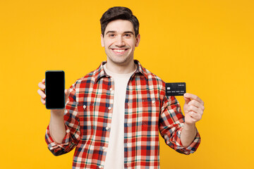 Wall Mural - Young happy man he wears red checkered shirt casual clothes using blank screen mobile cell phone hold credit bank card shopping online order delivery booking tour isolated on plain yellow background.