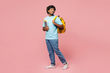 Wall Mural - Full body side view happy young Indian boy student wear blue t-shirt casual clothes backpack bag hold books look aside on area isolated on plain pink background High school university college concept