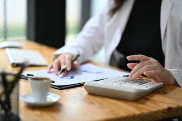 Wall Mural - Cropped shot female accountant making calculations and preparing financial data report at desk