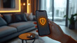 © gankevstock - Hand holding smartphone with security icon in modern living room