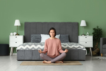 Poster - Young woman meditating while sitting on floor in bedroom