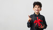 © Kanlayarawit - A cute and happy Arab boy holding a black gift box with red ribbon and pointing a point forefinger up to copy space on white background.