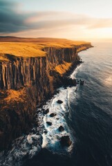 Wall Mural - A stunning aerial view of a dramatic cliff face along a rugged coastline, with the sun setting over the ocean.